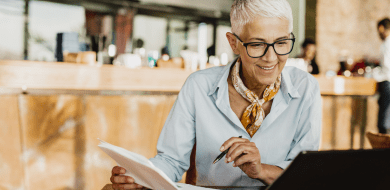 Femme senior portant des lunettes et un foulard jaune se renseignant sur le retour à l'emploi des seniors en France