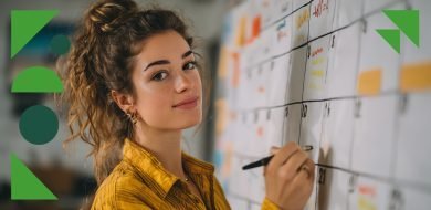 Une jeune femme souriante, debout devant un grand calendrier mural, planifie des publications à l’aide d’un marqueur — symbole de l’organisation et des missions quotidiennes d’un community manager.