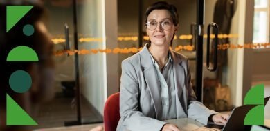 Femme souriante en tenue professionnelle, assise à un bureau avec un ordinateur portable, lors d’un entretien dans un environnement de bureau moderne.