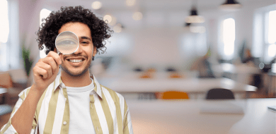 Personne souriante tenant une loupe devant un œil dans un espace de travail lumineux, illustrant l’analyse, l’innovation et la vision stratégique à l'ifocop.