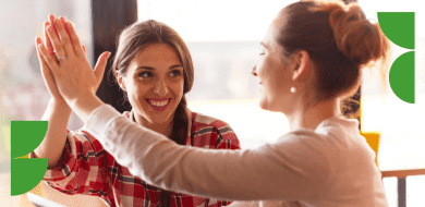 Deux femmes souriantes se font un high-five, illustrant un moment d’encouragement et de réussite partagée.