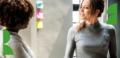 Deux personnes échangent lors d’une visite, devant un mur avec des post-it, illustrant un moment de découverte et d’orientation professionnelle.