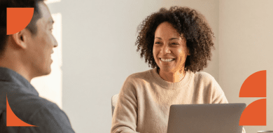 Deux professionnels échangent avec le sourire autour d'un ordinateur portable lors d'un entretien RH en entreprise.